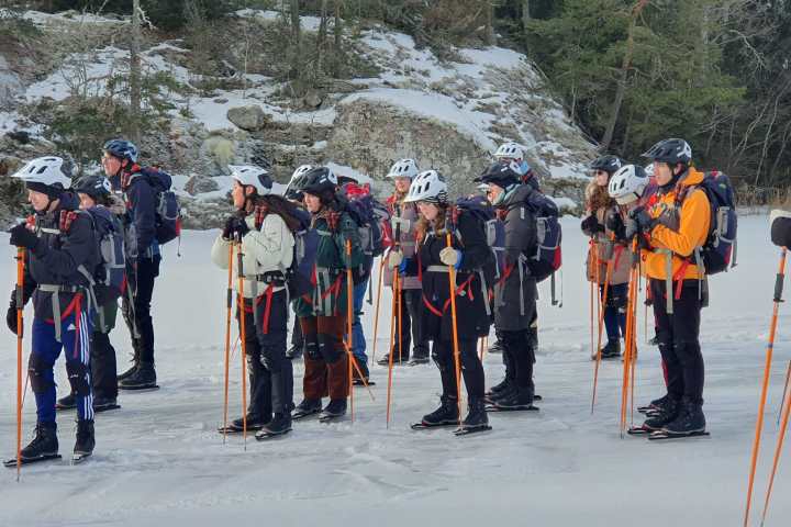 Group of people in winter gear with helmets and poles stand on snowy ground.