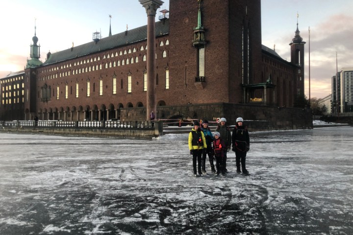 Group of people ice skating in front of a large historic brick building at dusk.