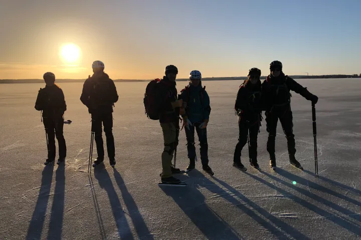 Silhouettes of five people with poles on a frozen lake at sunset.