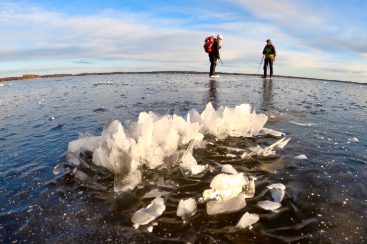 Two ice skaters observe an ice formation on a frozen lake