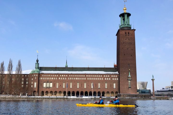 a large clock tower sitting next to a body of water with Stockholm City Hall in the background