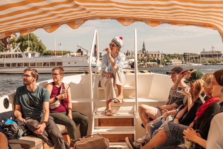 Group of people relaxing on a boat with a striped canopy on a sunny day.
