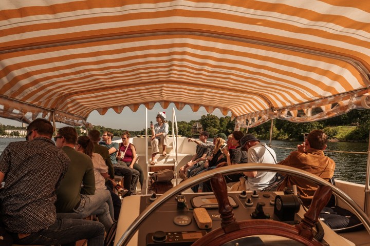 People on a boat with striped canopy, trees in the background.