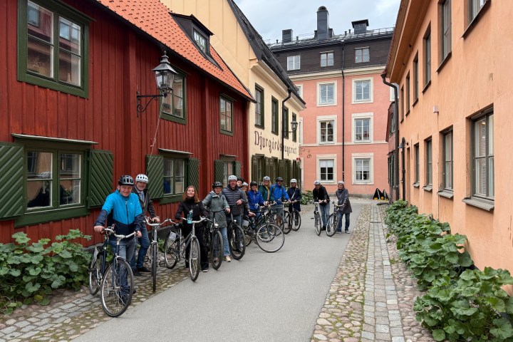 Group of cyclists paused on a cobblestone street between colorful buildings.