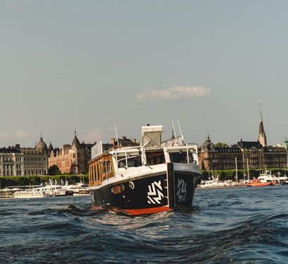 Boat on wavy water with historic buildings in the background on a sunny day.